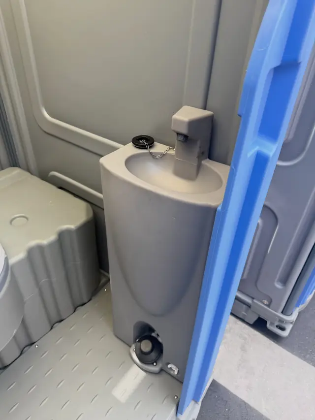 Inside a deluxe portable toilet with a hand sink beside the seat