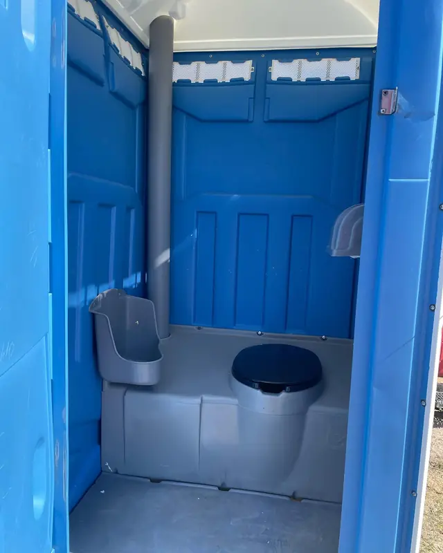 Inside a blue standard porta potty showing the urinal and toilet seat