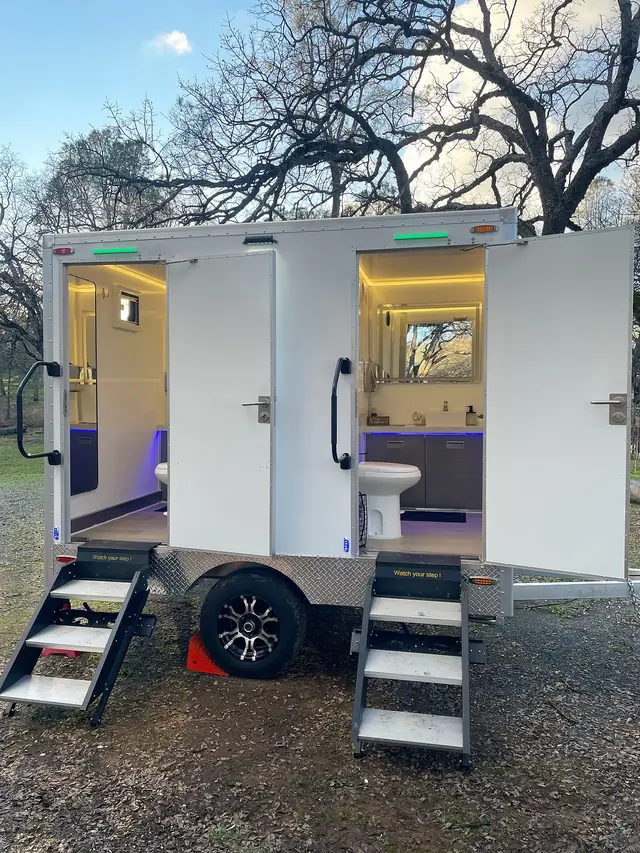Two-stall restroom trailer with its doors open and interior lights on